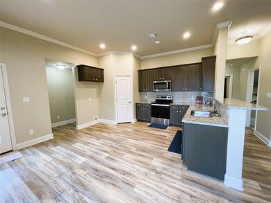 Kitchen with light stone countertops, light wood-type flooring, backsplash, appliances with stainless steel finishes, and sink
