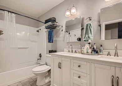 Full bathroom featuring double vanity, shower / bath combo with shower curtain, and light tile patterned flooring