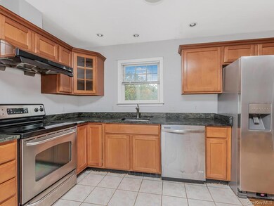 Kitchen featuring stainless steel appliances, exhaust hood, brown cabinets, light tile patterned flooring, and recessed lighting