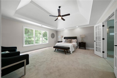 Bedroom with a tray ceiling, french doors, light colored carpet, crown molding, and a ceiling fan