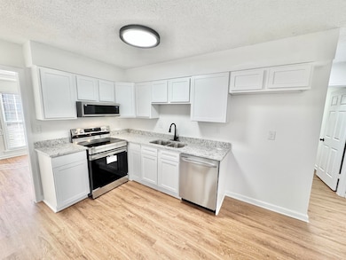Kitchen featuring stainless steel appliances, white cabinets, a textured ceiling, and light wood-style floors