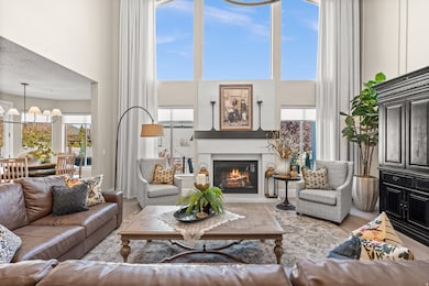 Living area with a high ceiling, healthy amount of natural light, a glass covered fireplace, wood finished floors, and a chandelier