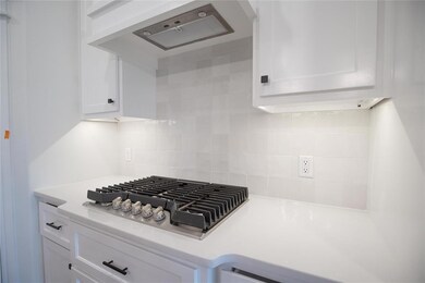 Kitchen view of stainless steel gas cooktop, exhaust hood, white cabinets, light countertops, and decorative backsplash