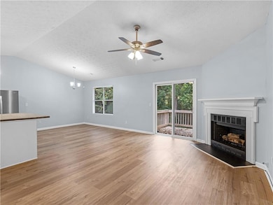 Unfurnished living room with light wood finished floors, a textured ceiling, a fireplace with raised hearth, vaulted ceiling, and a ceiling fan