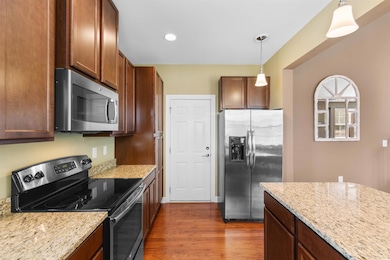 Kitchen with hanging light fixtures, dark wood-type flooring, stainless steel appliances, and light stone countertops
