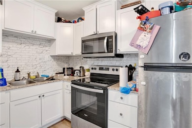 Kitchen featuring appliances with stainless steel finishes, decorative backsplash, and white cabinets