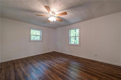 Unfurnished room with healthy amount of natural light, dark wood-style flooring, baseboards, and a textured ceiling