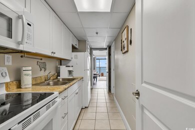 Kitchen featuring white appliances, a sink, light tile patterned floors, white cabinetry, and a paneled ceiling