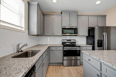 Kitchen with gray cabinets, appliances with stainless steel finishes, light stone counters, light wood-style floors, and backsplash