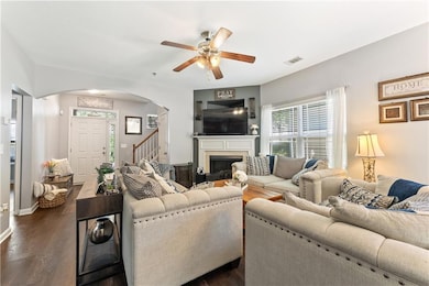 Living room featuring arched walkways, ceiling fan, a fireplace, stairs, and dark wood-type flooring