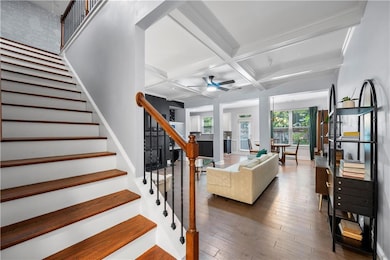 Living area with coffered ceiling, a ceiling fan, stairway, wood finished floors, and beam ceiling