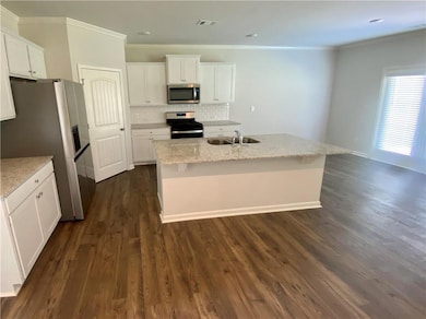 Kitchen with stainless steel appliances, white cabinets, wood finished floors, backsplash, and light stone countertops