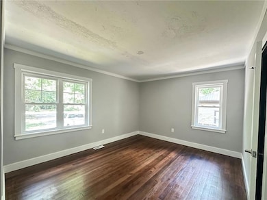 Empty room featuring dark wood-style flooring, baseboards, crown molding, and a textured ceiling