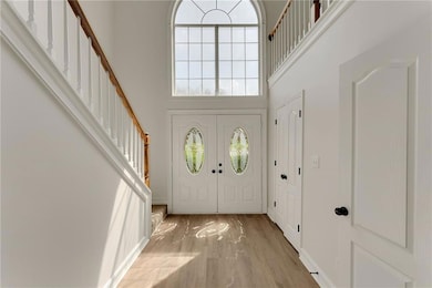 Foyer entrance with a high ceiling, stairs, and light wood-style flooring