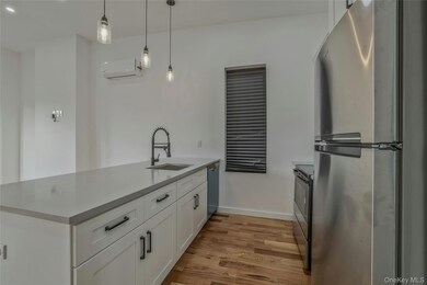 Kitchen featuring appliances with stainless steel finishes, a peninsula, white cabinets, light wood-style floors, and decorative light fixtures