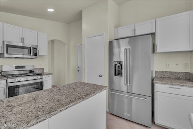 Kitchen featuring appliances with stainless steel finishes, light stone countertops, light tile patterned flooring, arched walkways, and white cabinets