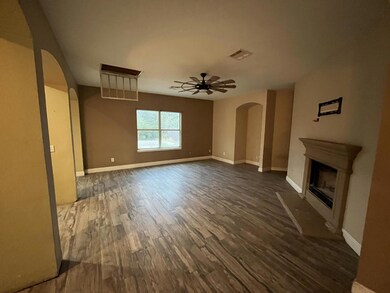Unfurnished living room featuring arched walkways, a fireplace with raised hearth, dark wood-style floors, and ceiling fan