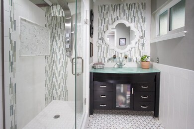 Sumptuously remodeled en suite bathroom with modern vanity topped with tempered aqua glass, matching faucet, framed dressing mirror, custom tiled frameless glass-enclosed step-in shower, tiled floors and private backyard access.