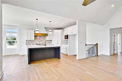 Kitchen with light countertops, a sink, white cabinetry, premium range hood, and built in microwave
