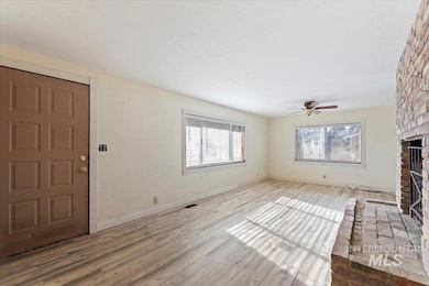 Unfurnished living room with a brick fireplace, plenty of natural light, wood finished floors, and a ceiling fan