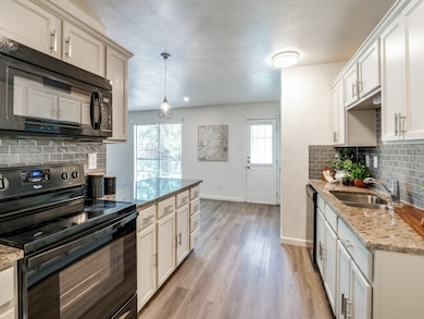 Kitchen featuring backsplash, black appliances, light stone countertops, and decorative light fixtures