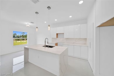 Kitchen featuring sink, hanging light fixtures, decorative backsplash, light stone countertops, and white cabinetry