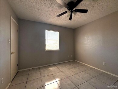 Empty room with a textured ceiling, light tile patterned floors, baseboards, and a ceiling fan