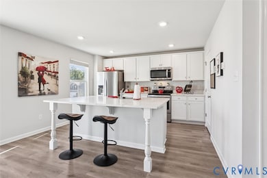 Kitchen featuring appliances with stainless steel finishes, white cabinetry, light wood-style flooring, a breakfast bar, and an island with sink