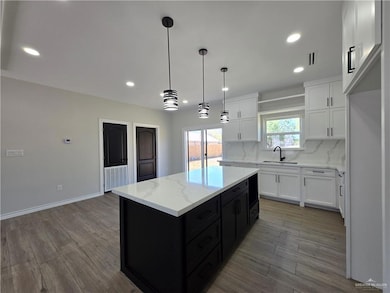 Kitchen with dark cabinets, white cabinets, hanging light fixtures, light wood-style flooring, and tasteful backsplash