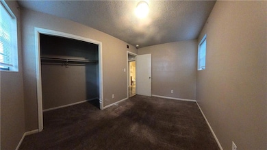 Unfurnished bedroom featuring a textured ceiling, a closet, and dark colored carpet