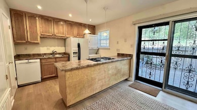 Kitchen featuring a peninsula, recessed lighting, white appliances, decorative light fixtures, and light wood-style floors