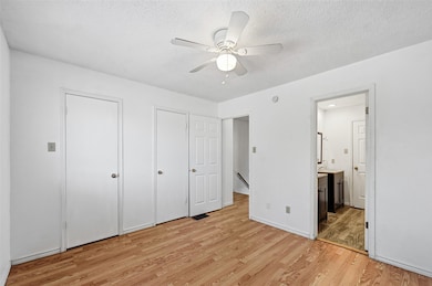 Unfurnished bedroom featuring multiple closets, light wood-style floors, a ceiling fan, a textured ceiling, and ensuite bathroom
