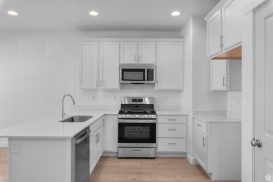 Kitchen featuring light wood-type flooring, a sink, light countertops, a peninsula, and stainless steel appliances