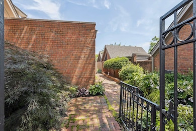 Featuring a Brick Path Surrounded by Lush Landscaping, Mature Plantings, and a Decorative Iron Gate—Creating a Welcoming and Private Entrance to the Home.