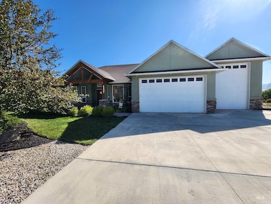 View of front of home with stone siding, driveway, a garage, a front lawn, and covered porch