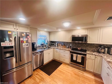 Kitchen with light stone counters, light hardwood / wood-style floors, crown molding, and appliances with stainless steel finishes