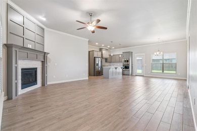 Unfurnished living room with crown molding, light wood-style floors, a fireplace, ceiling fan, and a chandelier