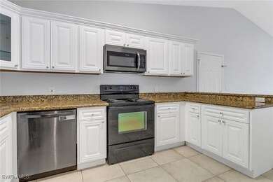 Kitchen featuring stainless steel appliances, white cabinetry, dark stone countertops, light tile patterned floors, and lofted ceiling