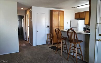 Kitchen featuring brown cabinetry, a breakfast bar area, light countertops, dark carpet, and freestanding refrigerator