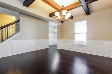 Unfurnished dining area featuring beam ceiling, a chandelier, dark wood-type flooring, coffered ceiling, and wainscoting
