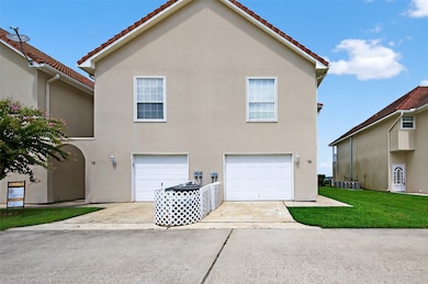 This photo features a modern two-story duplex with a beige exterior and red-tiled roof. It has a single-car garages and a paved driveway. The property is well-maintained with a small lawn area