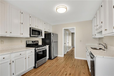 Spacious galley-style kitchen with ample white cabinetry, sleek stainless steel appliances, neutral countertops, and warm wood-look flooring, offering a clean and functional cooking space.