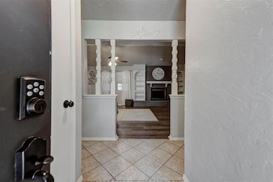 Entrance foyer featuring light tile patterned floors, a textured wall, a brick fireplace, baseboards, and a ceiling fan