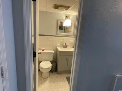 Bathroom featuring vanity, toilet, wainscoting, tile patterned floors, and a drop ceiling