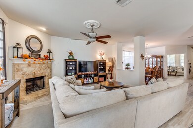 Living area with ceiling fan, a stone fireplace, and light wood-style floors