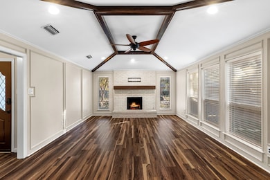 Unfurnished living room featuring dark wood finished floors, ceiling fan, a decorative wall, a brick fireplace, and crown molding