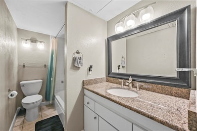 Full bathroom with a textured wall, shower / bath combo, light tile patterned floors, and vanity