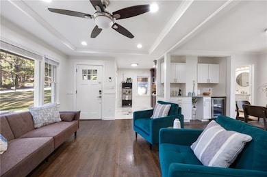 Living area with a tray ceiling, healthy amount of natural light, dark wood-style flooring, recessed lighting, and crown molding