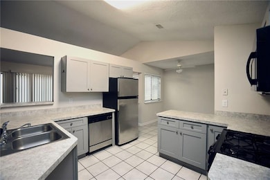 Kitchen with gray cabinetry, light countertops, black appliances, lofted ceiling, and light tile patterned floors