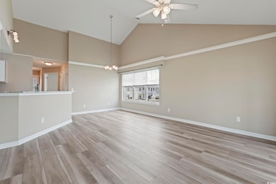 Unfurnished living room featuring high vaulted ceiling, a ceiling fan, light wood-style flooring, a chandelier, and baseboards